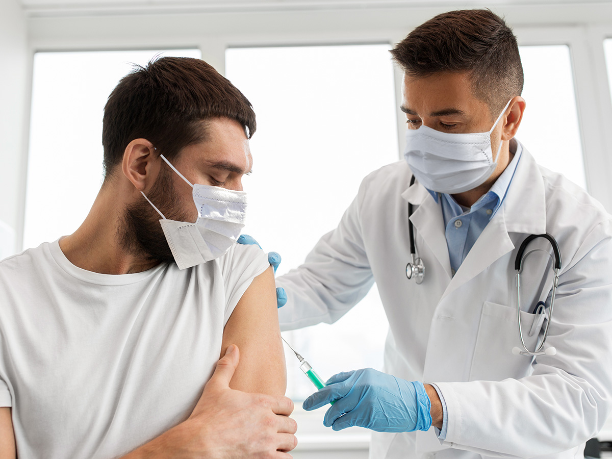 Man getting a shot by a male doctor at the doctor’s office.