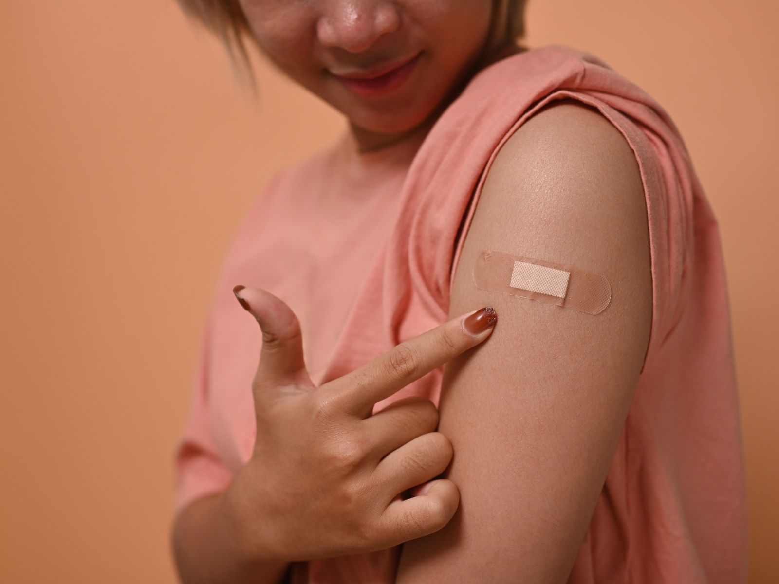 young woman happily pointing to her bandage, post vaccination